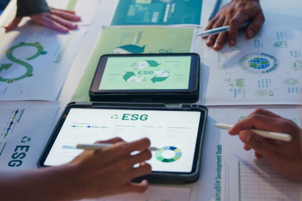 Two tablets showing ESG progress dashboards among printed sustainability charts on a meeting table